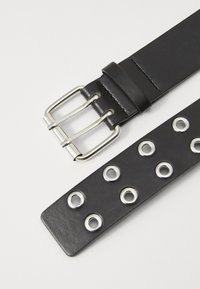 Ceinture en cuir noir avec une boucle à double ardillon en argent. Présente des œillets en métal ronds le long de la sangle pour un ajustement de taille.