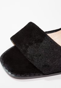 Sandale noire en velours avec bride large et bout carré sur fond blanc.