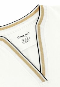 Witte blouse met een V-hals, voorzien van gouden en zwarte gestreepte afwerking. Label zegt "vieux jeu," met maat EU XS en gemaakt in Turkije.