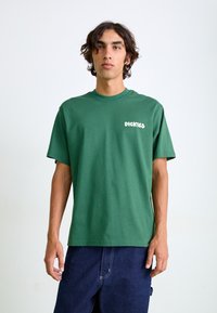 Grünes Baumwoll-T-Shirt mit kurzen Ärmeln, rundem Ausschnitt und weißem 'DICKIES'-Logo auf der linken Seite. Schlichter Schnitt.