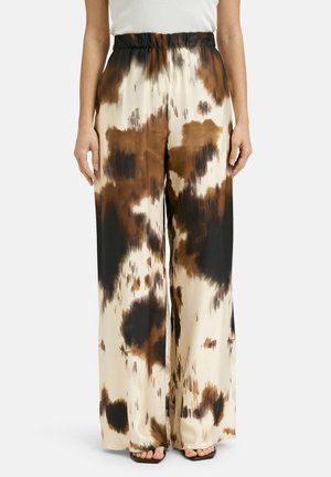 Woman wearing high-waist wide-leg pants with brown, black, and cream abstract tie-dye pattern and a white sleeveless top.