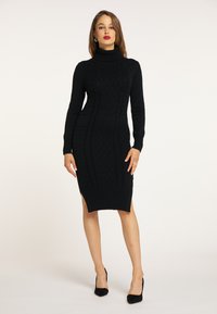 Abito nero lavorato a maglia con collo alto, motivo a treccia elaborato, maniche lunghe e spacchi laterali, che offre una silhouette aderente.