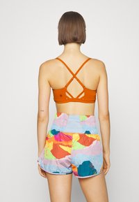 Top desportivo laranja com alças cruzadas e recorte nas costas, combinado com calções multicoloridos com padrões abstratos em tons vibrantes.