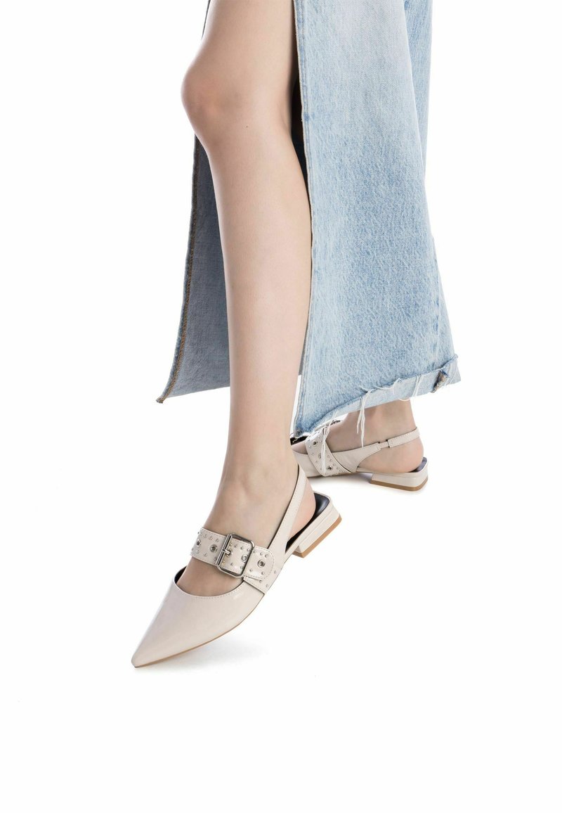 Zapatos slingback de punta en cuero beige, con una correa ancha que presenta una hebilla decorativa y tachuelas metálicas, combinados con una falda de mezclilla.