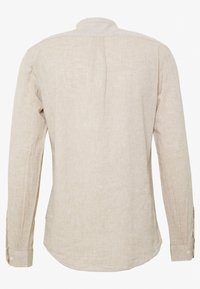 Camisa beige de manga larga hecha de tela ligera, con cuello puntiagudo, puños abotonados y dobladillo redondeado con una textura sutil.