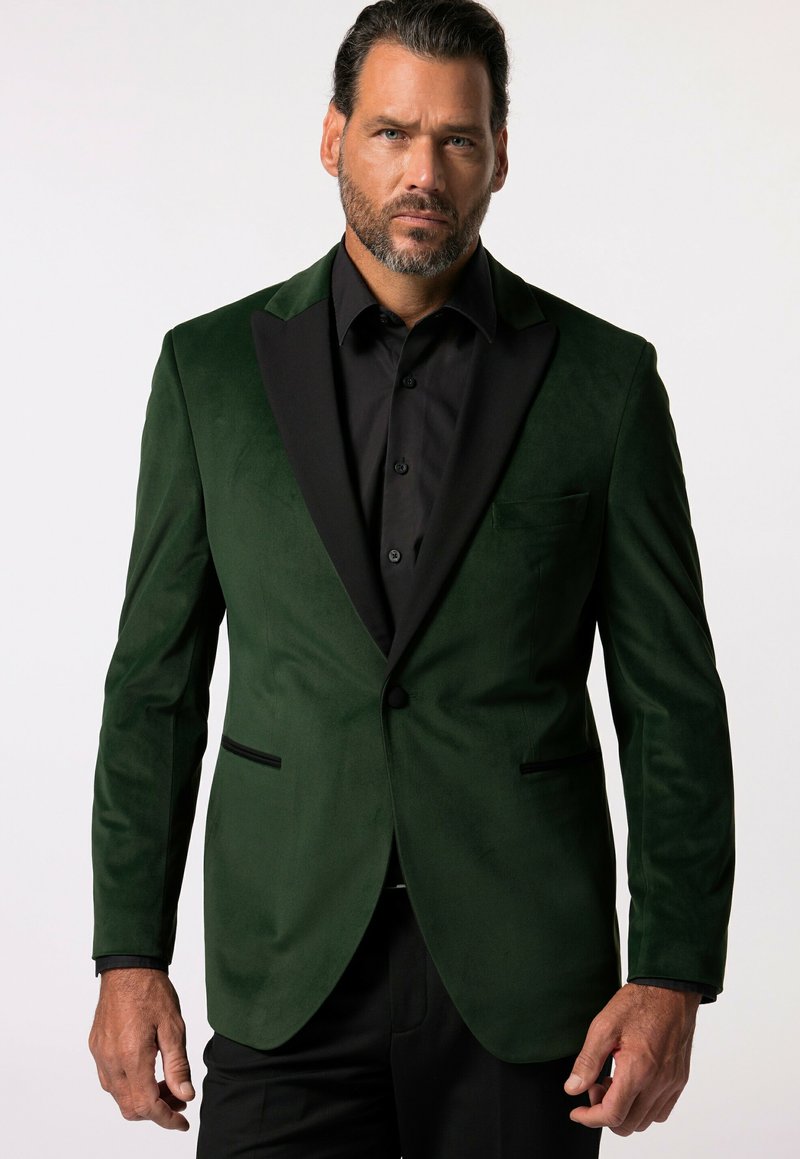 Blazer verde in velluto con rever in satin nero, chiusura a un bottone, tasche a pattina e texture liscia, abbinato a una camicia nera.