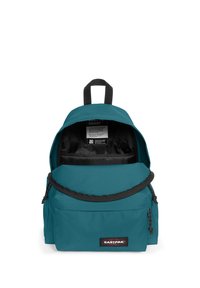 Zaino turchese con scomparto principale con zip, tasca frontale piatta e patch con logo. Realizzato in tessuto resistente e dotato di manico superiore per il trasporto.