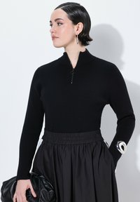 Zwarte geribbelde trui met een hoge kraag en een halve rits, gecombineerd met een zwarte rok met elastische taille. Heeft een gestructureerde afwerking en een soepele stof.