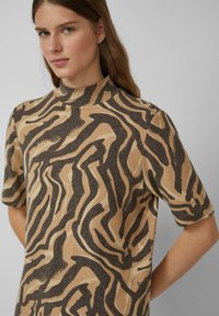 Lühikeste varrukatega särk kõrge kaelusega, millel on laineline must ja beež abstraktne muster pehmel, tekstuurilisel kangal.