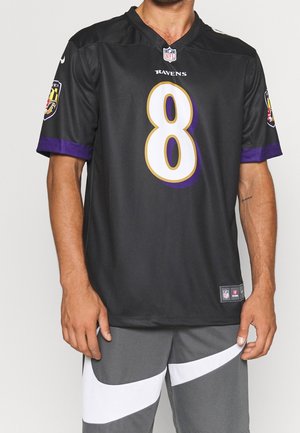 Mand iført en sort Baltimore Ravens NFL-trøje med nummer 8 og grå sportsshorts med hvide diagonale striber.