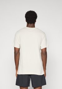Lys beige T-shirt med kort ærme, rund hals og en afslappet pasform. Glat tekstur uden synlige mønstre eller dekorationer.