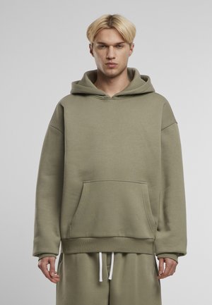 Sweat à capuche vert olive en tissu doux, avec une poche frontale, un cordon de serrage à la capuche, et des poignets côtelés. Coupe décontractée avec des manches larges.