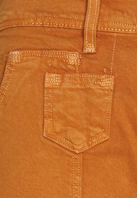 Orange Denimstoff mit einer Gesäßtasche. Nähte in passender Farbe, mit einer leicht strukturierten Oberfläche und einer charakteristischen Form.