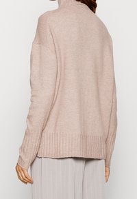 Jasnoróżowy sweter z wysokim kołnierzem, prążkowanym wykończeniem i długimi rękawami. Wykonany z miękkiego, teksturowanego materiału dzianinowego. Prosty i luźny fason.