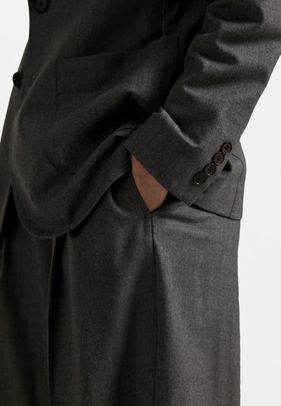 Temno siva obleka po meri z žepom, ki se ponaša z gladko teksturo in štirimi gumbi na manšeti. Dobro prilegajoča zasnova.