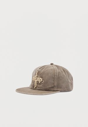 Gorra de béisbol de gamuza marrón con visera plana y bordado en relieve color canela que presenta un texto estilizado en el panel frontal.