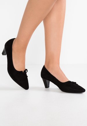 Chaussures à talons hauts en daim noir avec un bout pointu et un petit nœud en accent, présentant une finition texturée et une hauteur de talon modérée.