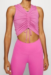 Top corto rosa con texture a coste, caratterizzato da un scollo a V e dettagli arricciati al centro, abbinato a leggings rosa a vita alta.