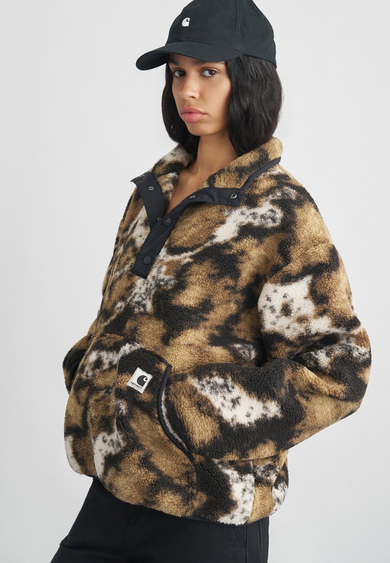 Pulôver de fleece com padrões castanho e preto, com gola alta, fecho de pressão preto e bolsos laterais. Inclui um patch de logótipo na parte frontal.