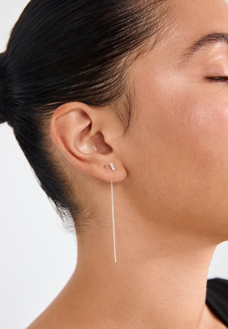 Hõbedased kõrvarõngad, millel on naastdisain lühikese kettlangusega, rõhutades minimalistlikku kuju ja siledat, poleeritud pinda.