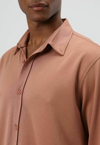 Knopfhemd aus gedämpftem rosa Stoff, mit klassischem Kragen, zwei Frontknöpfen, glatter Textur und figurbetontem Design.