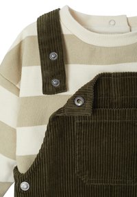 Olive green corduroy overalls with silver snap buttons paired with a beige and cream striped long-sleeve shirt. Textured fabric details visible.