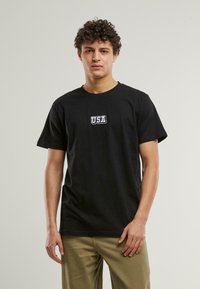 Svart bomull t-skjorte med hvit "USA" logo på brystet. Korte ermer, klassisk rund hals og avslappet passform.