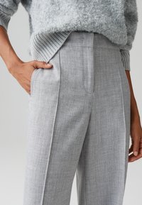 Lichtgrijze, op maat gemaakte broek met een gestructureerde stof, zijzakken en een recht model, gecombineerd met een gezellige grijze gebreide trui.