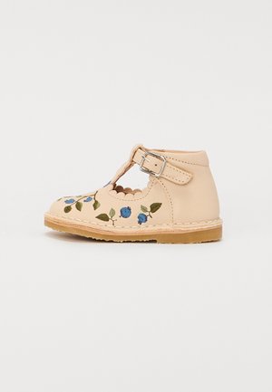Scarpa in pelle color tan con ricami floreali in blu e verde, tagli a scallop e una fibbia laterale. Suola piatta con bordo cucito.