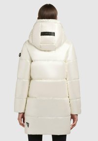 Padded white parka with a high collar and hood, featuring a black logo patch at the back and a triangular brand tag on the side.