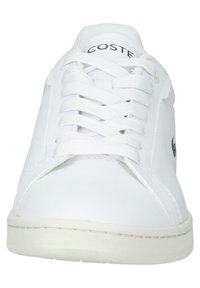 Baskets en cuir blanc avec lacets blancs, nom de la marque "Lacoste" sur la languette et logo crocodile vert sur le côté.