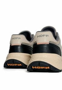 Un paio di sneakers beige e nere con suole texturizzate, logo arancione "HOFF" sul tallone e sulla suola, mostrate da dietro su uno sfondo bianco.