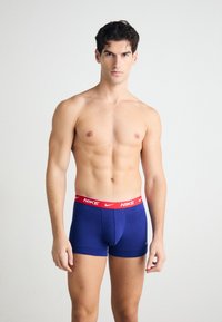 Marineblaue Boxershorts mit einem roten Nike-Logo-Bündchen. Der Stoff wirkt glatt und enganliegend und zeigt ein strukturiertes Design.