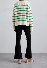 Pull en maille à base crème avec des rayures vertes, associé à un pantalon évasé noir taille haute et des sandales beiges à talons blocs.