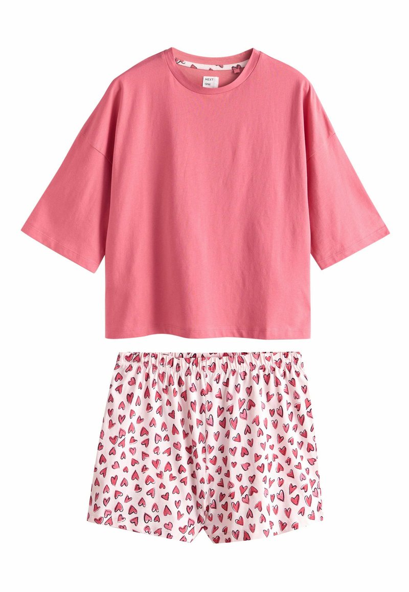 Lyserød bomulds T-shirt med korte ærmer kombineret med hvide shorts med et gentaget mønster af lyserøde hjerter og elastisk talje.