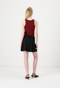 En tettsittende burgunderfarget singlet kombinert med et svart plyndred skjørt, som viser et strømlinjeformet design og kontrasterende teksturer. Sorte hæler fullfører antrekket.