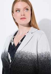 Ombre bleiseri, joka siirtyy vaaleanharmaasta mustaan, hienovaraisilla pistekoristeilla. Varustettu lovettulla kauluksella ja yksittäisellä napilla.