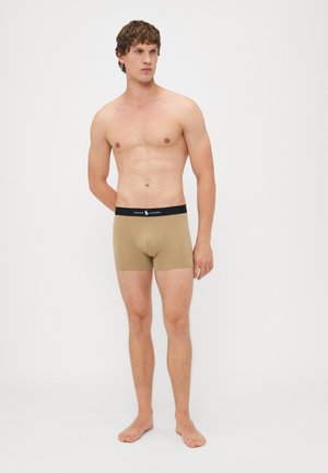 Beżowe slipy wykonane z miękkiej bawełny, z czarnym elastycznym pasem, na którym widnieje logo "Ralph Lauren". Minimalistyczny design i dopasowany kształt.
