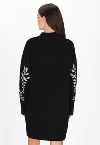 Rochie-pulover neagră, tricotată, cu gât înalt, decorată cu broderie cu frunze argintii pe mâneci. Designul este supradimensionat și confortabil.