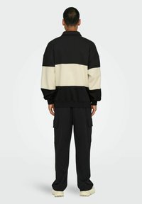 Schwarz- und cremefarbener, farbblockierter Pullover mit Kragen, kombiniert mit schwarzen Cargo-Hosen mit Seitentaschen, im lässigen Schnitt gestaltet.