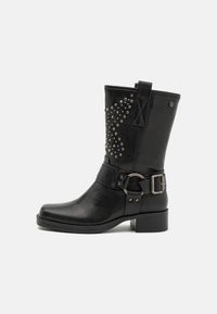 Bota de cuero negra a nivel del tobillo con diseño de tachuelas en el costado, correa con hebilla, punta redonda y tacón bajo. Acabado texturizado.