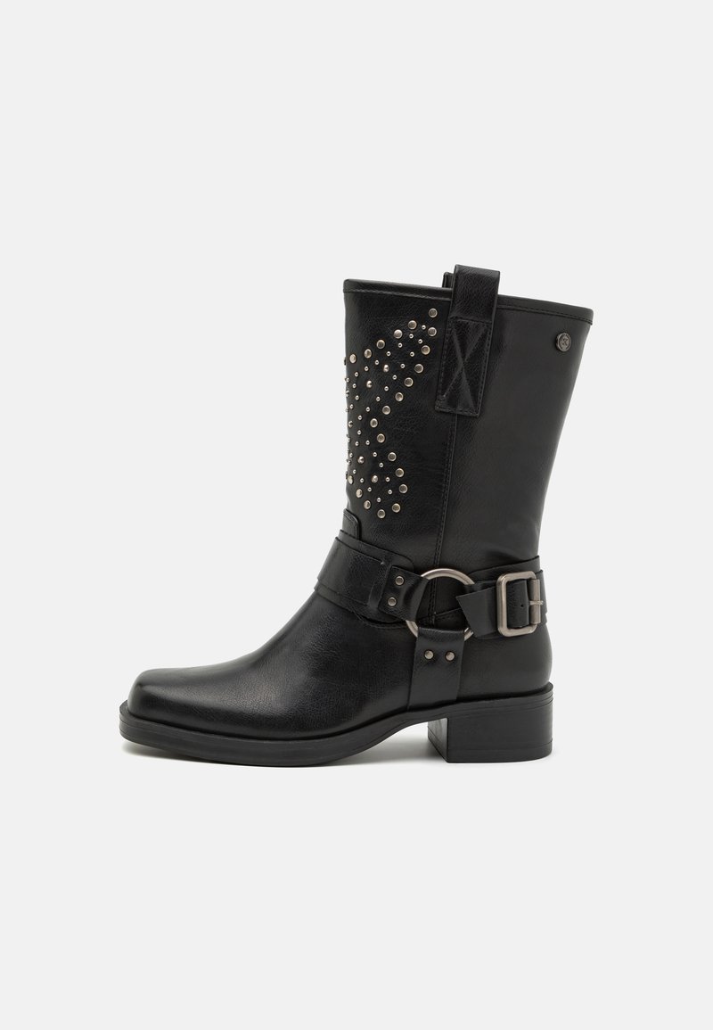 Bota de cuero negra a nivel del tobillo con diseño de tachuelas en el costado, correa con hebilla, punta redonda y tacón bajo. Acabado texturizado.