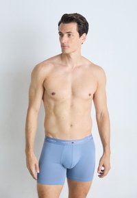 Boxers bleus en tissu lisse, avec une taille élastique portant le texte "TOMMY HILFIGER". Design ajusté, longueur mi-cuisse.