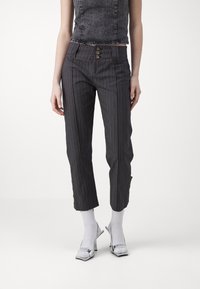 Pantaloni grigi a righe con design alto in vita, dotati di tre bottoni e lunghezza cropped, abbinati a tacchi metallici e calzini bianchi.