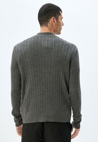 Suéter gris de canalé que presenta mangas largas y un cuello redondo. La textura es suave y tiene un patrón vertical constante en toda su superficie.