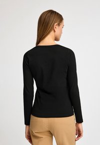 Svart långärmad topp i mjukt tyg, med rund halsringning och en figursydd passform. Sömlös rygg med minimal sömnadsdetalj.