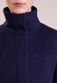 Navy blue wool-blend coat with a high collar, featuring a smooth texture and clean design, highlighting minimal seams and a modern silhouette.
