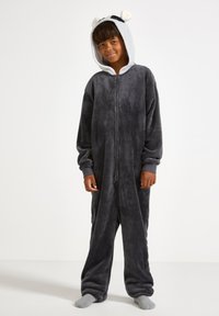 Une combinaison en polaire grise avec fermeture éclair, dotée d'une capuche sur le thème des pandas avec des oreilles et des poignets côtelés. Texture douce et coupe décontractée.