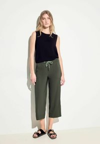 Top sans manches noir au look texturé, associé à un pantalon court vert olive avec une taille à cordon et deux poches avant. Sandales noires.