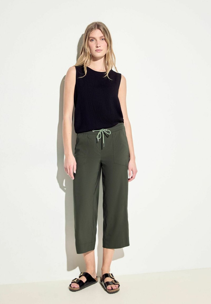 Top sans manches noir au look texturé, associé à un pantalon court vert olive avec une taille à cordon et deux poches avant. Sandales noires.